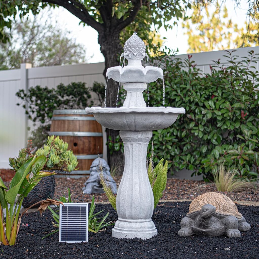 Tall white solar pedestal garden fountain with cascading water, turtle statue, and plants in a small backyard.