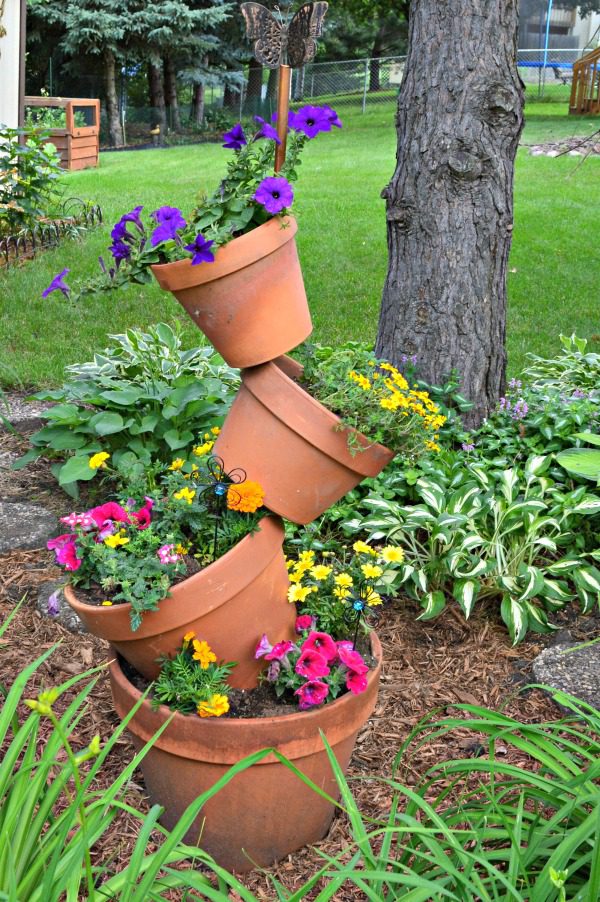 Whimsical small garden with stacked tilted terracotta pots filled with colorful flowers beside a tree